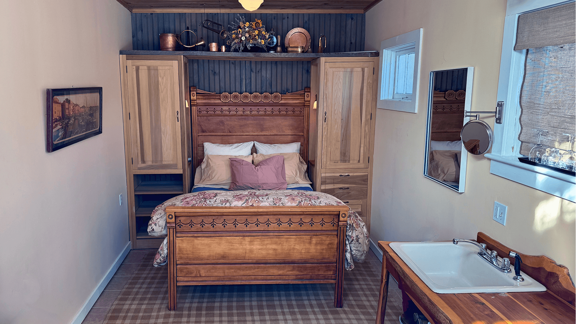 A cozy, minimalist bedroom featuring a wooden bed, floral bedding, and a small sink with a mirror.