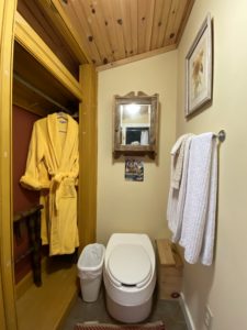 white toilet with garbage can beside, closet with yellow robe hanging, towel rack with white towels