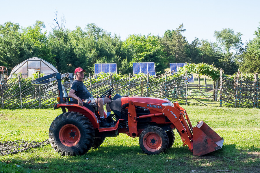 farmer relaxing on a red tractor in front of an extensive garden and solar panels