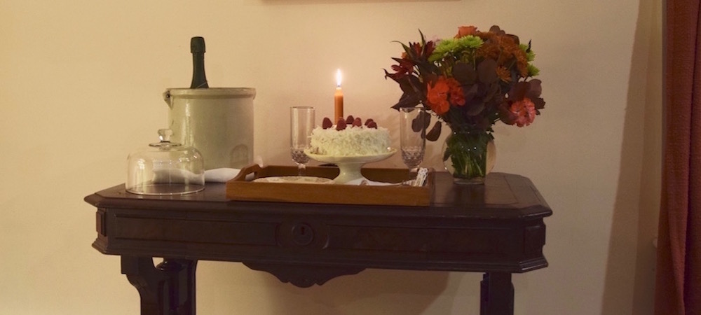 flowers, wine and cake with coconut frosting and strawberries placed on a small table