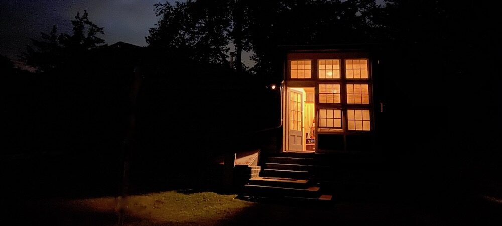 cottage a night with lights shining with woods in background