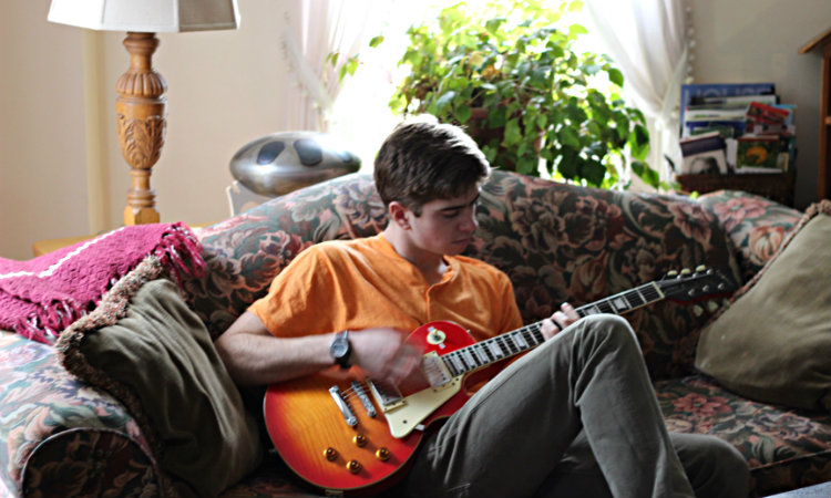young man in orange shirt playing guitar on sofa in parlor